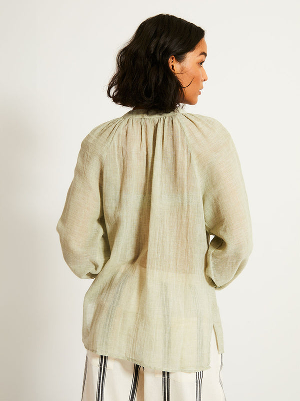Back of a Woman Standing Wearing lemlem MITA Blouse featuring airy gauze fabric in a delicate earthy sage color