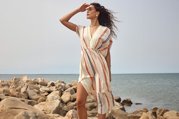 Woman standing wearing lemlem handwoven dress featuring colorful striped pattern on cream background