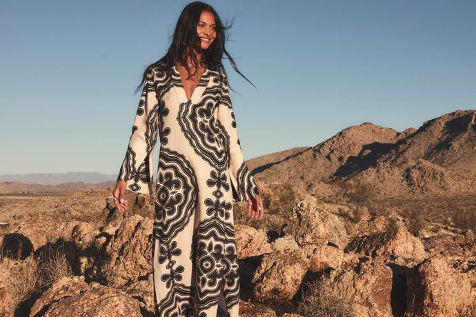 Woman sitting on stones wearing lemlem linen column dress featuring blakc pattern on cream background