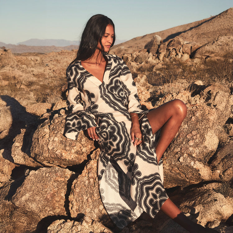 Woman in a patterned dress sitting on rocks in a desert landscape