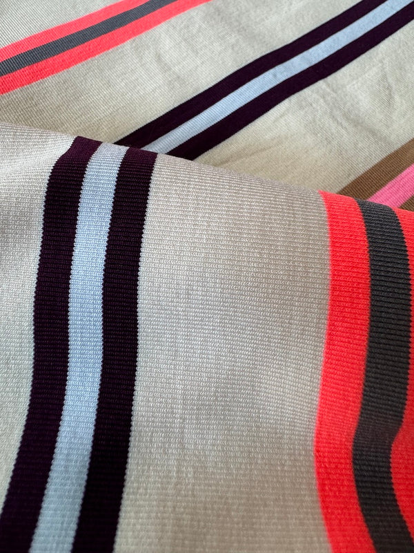 Close up on lemlem niyoni swim fabric featuring multicolored stripes with playful pops of bright yellow citrus, plum, light blue, neon pink, ochre, and orange—set against a soft vanilla-toned ground.
