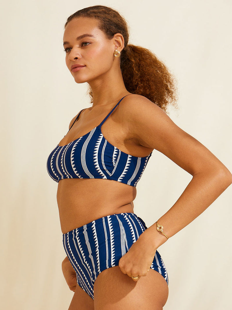 Woman standing with her hand by her hips wearing the Nunu bralette swim top in blue with white triangles and stripes