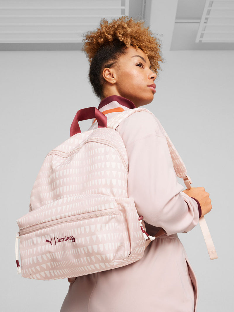 Woman Standing wearing  lemlem x Puma Backpack Featuring lemlem triangle pattern in rose quartz and white colors and puma x lemlem logo in red color and lemlem x Puma Jumpsuit