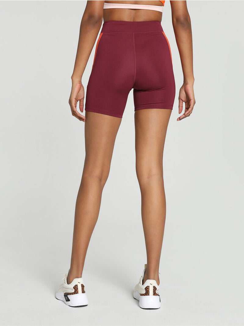 Back View on Legs of a woman standing wearing Puma x lemlem Biker Shorts Featuring Team Regal Red Color and color block details on hips in Warm White and Cayenne Pepper Colors
