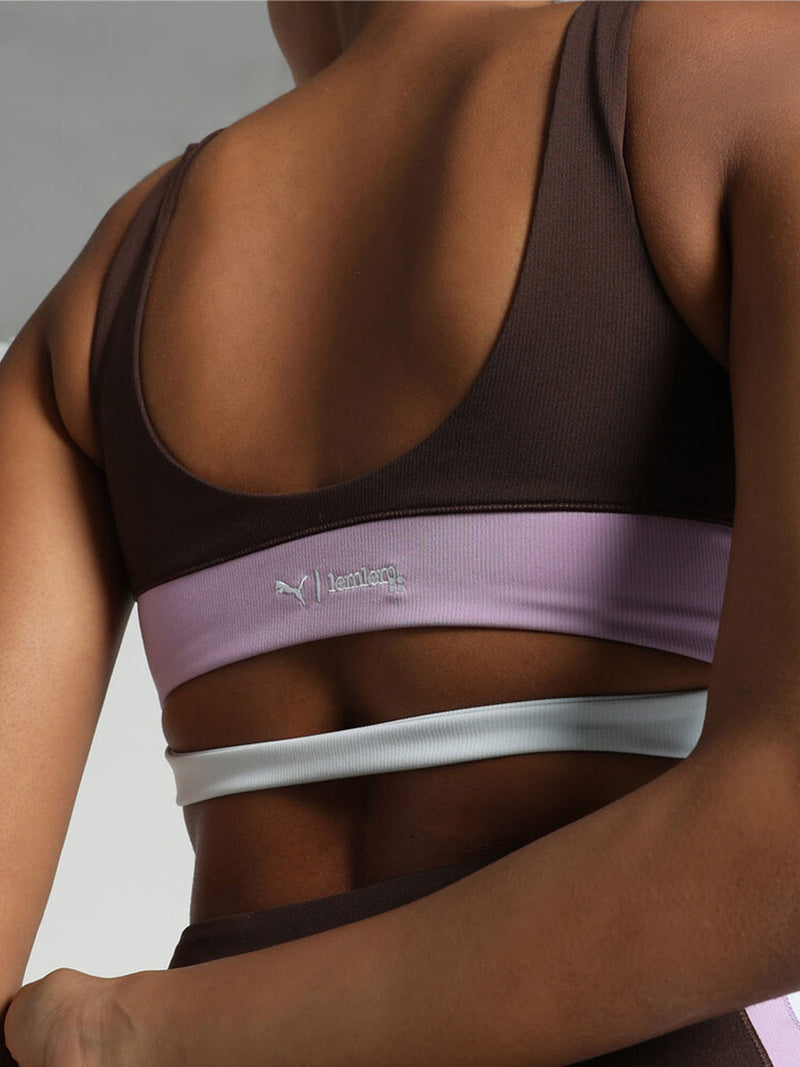 Back View of a Woman Standing Wearing Puma x lemlem Crop Tank Featuring Dark Chocolate Color and Color Block Details on the Under Band in Violet and White colors and matching biker shorts