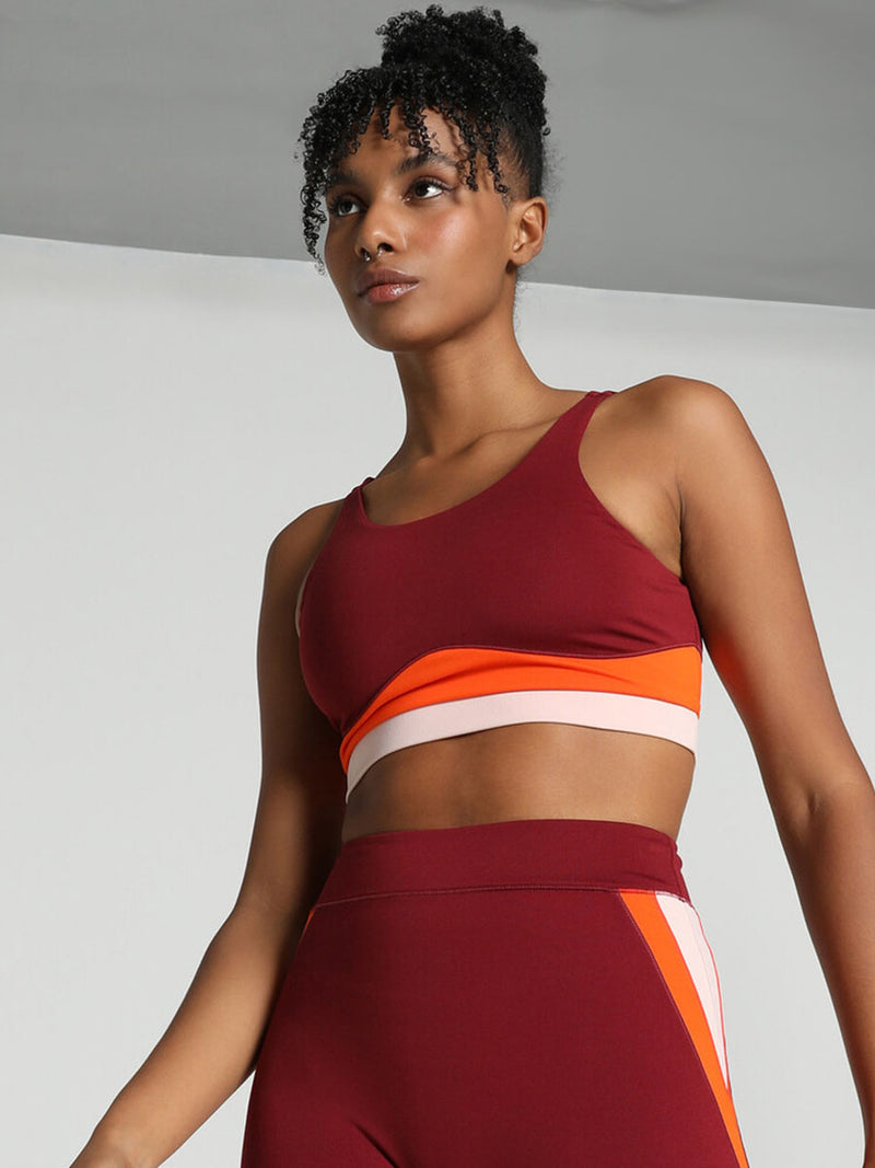 Woman Standing Wearing Puma x lemlem Crop Tank Featuring Team Regal Red Color and Color Block Details on the Under Band in Orange and White colors