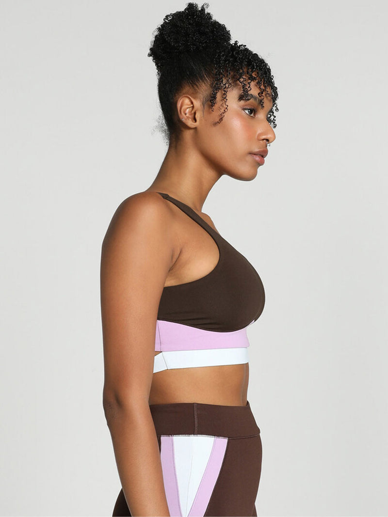 Side View of a Woman Standing Wearing Puma x lemlem Crop Tank Featuring Dark Chocolate Color and Color Block Details on the Under Band in Violet and White colors and matching biker shorts