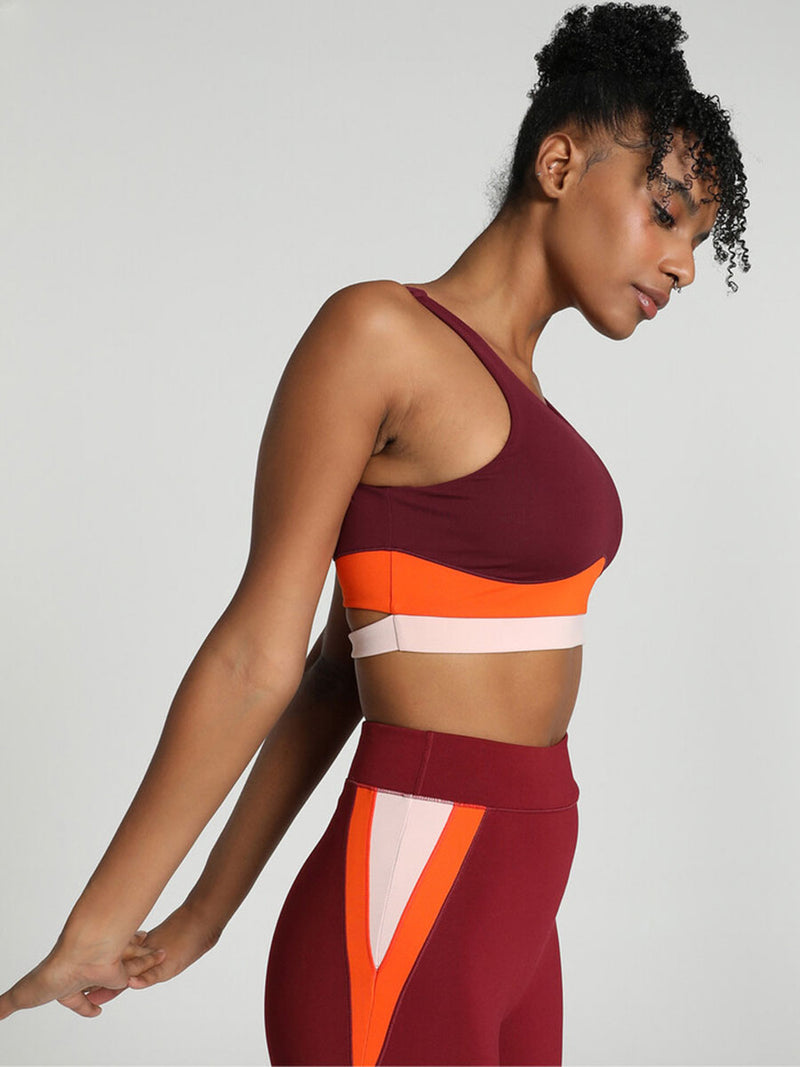 Side View of a Woman Standing Wearing Puma x lemlem Crop Tank Featuring Team Regal Red Color and Color Block Details on the Under Band in Orange and White colors and matching biker shorts