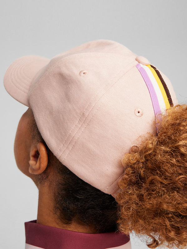 Back View of a Woman Standing Wearing Puma x lemlem Fleece Cap Featuring Rose Quartz Color and Puma x lemlem Logo on the Front and Puma x lemlem Jumpsuit