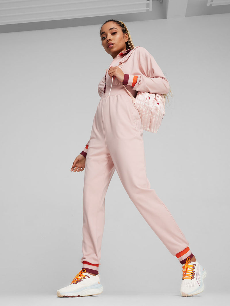 Woman Standing Wearing Puma x lemlem Rose Quartz Jumpsuit, Puma x lemlem Backpack and Puma x lemlem ForeverRUN Nitro Shoes featuring Icy Blue, Warm White, colors and color details in Cayenne Pepper and Team Regal Red
