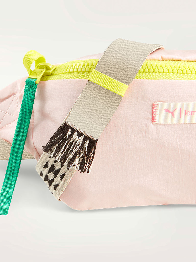 Close up on a lemlem waist bag in frosty pink color featuring color block zipper and lemlem triangle pattern strap
