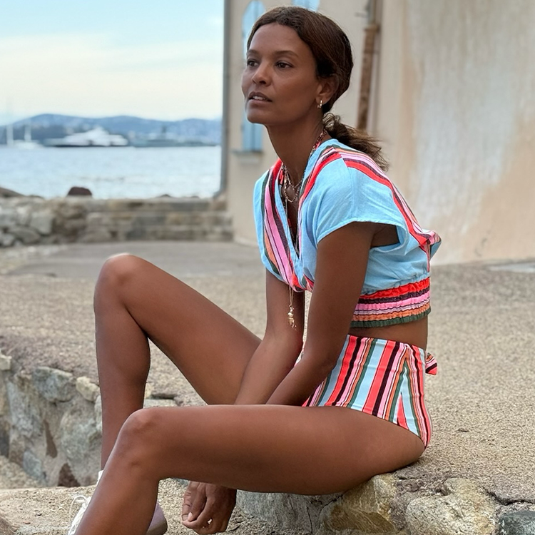 Liya Kebede sitting wearing lemlem ALIA Plunge top and ELSI High Waist Bottom featuring multicolor stripe pattern