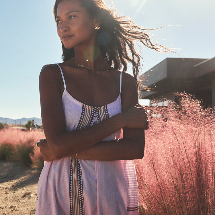 Woman in a pink handwoven lemlem dress standing in a field with pink grass and mountains in the background