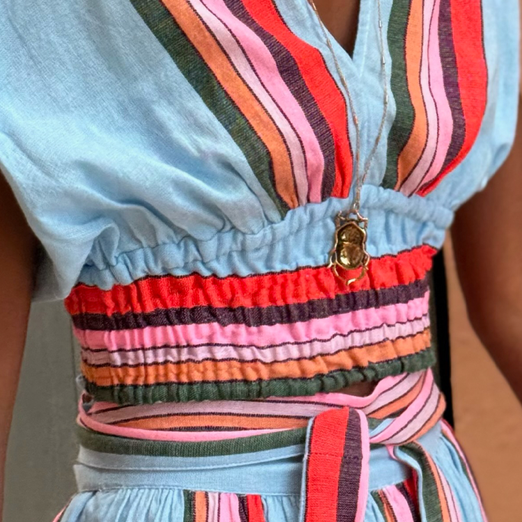 Close up on Liya Kebede sitting wearing lemlem ALIA Plunge top and  TOLA Wrap Skirt featuring multicolor stripe pattern