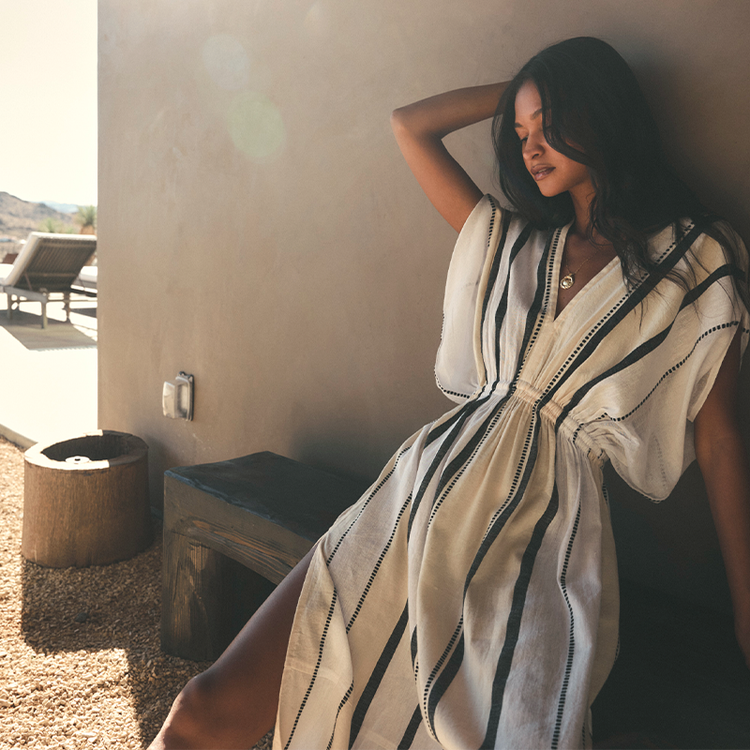 Woman in a striped lemlem handwoven dress leaning against a wall outdoors