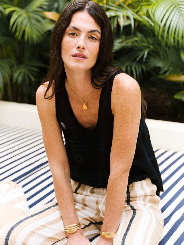 Woman sitting on a stripes outdoor sofa wearing a lemlem handwoven black tank top.