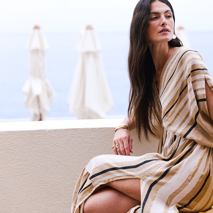 Woman sitting at a terrace in the South of France wearing a lemlem handwoven plunge neck dress in camel in white and black.