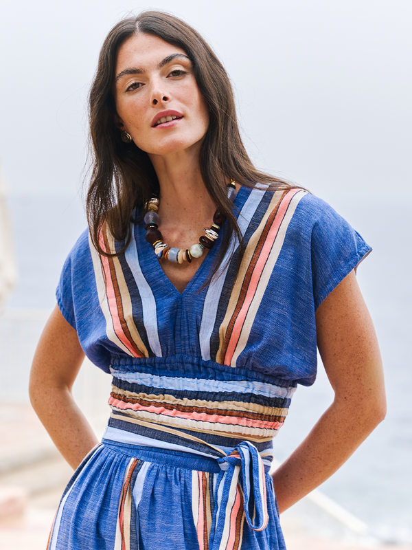 Woman standing with her arms in her back wearing a lemlem hand woven crop top and matching hand woven skirt in blue with light blue, camel, pink stripes. 