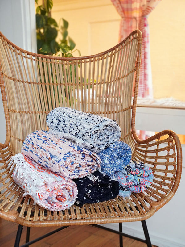Image of a straw chair with Coral, Pink Sky, White and Blue, Navy, Multi Blue and Black and Blue rugs laying on it.