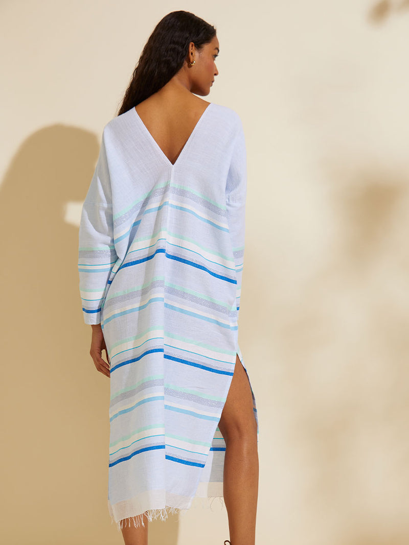 Back view of a woman standing  wearing the Ruki Long Sleeve Split Caftan featuring a mutli tonal stripe pattern in five shades of blue with silver and white accents.
