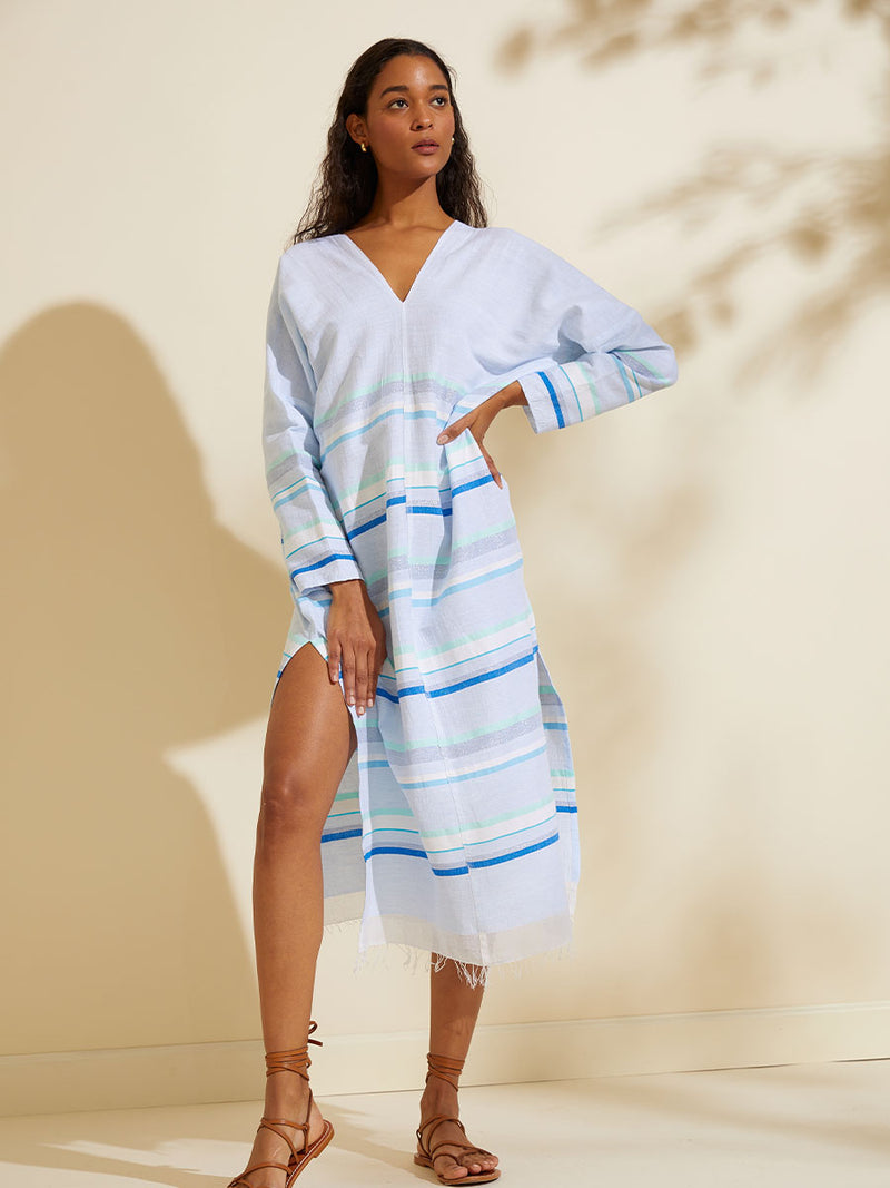 Woman standing wearing the Ruki Long Sleeve Split Caftan featuring a mutli tonal stripe pattern in five shades of blue with silver and white accents.
