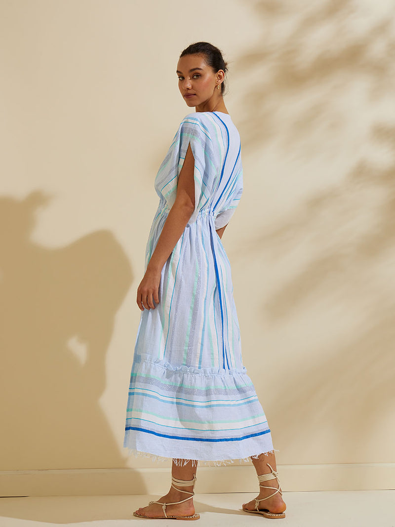 Side view of a woman standing wearing the Ruki Plunge Neck Dress featuring a mutli tonal stripe pattern in five shades of blue with silver and white accents.