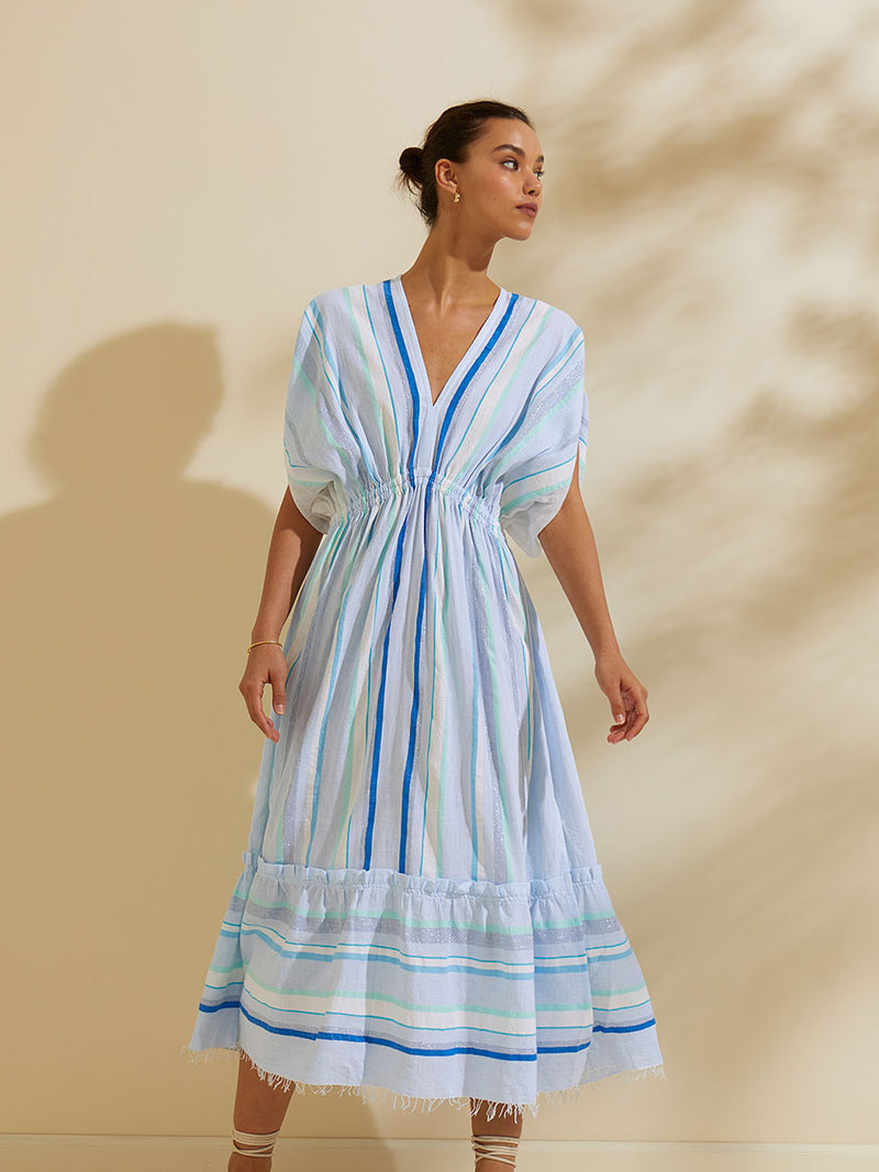 Woman standing  wearing the Ruki Plunge Neck Dress featuring a mutli tonal stripe pattern in five shades of blue with silver and white accents.