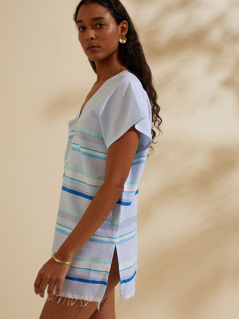 Side view of a woman standing wearing the Ruki Split Tunic featuring a mutli tonal stripe pattern in five shades of blue with silver and white accents.