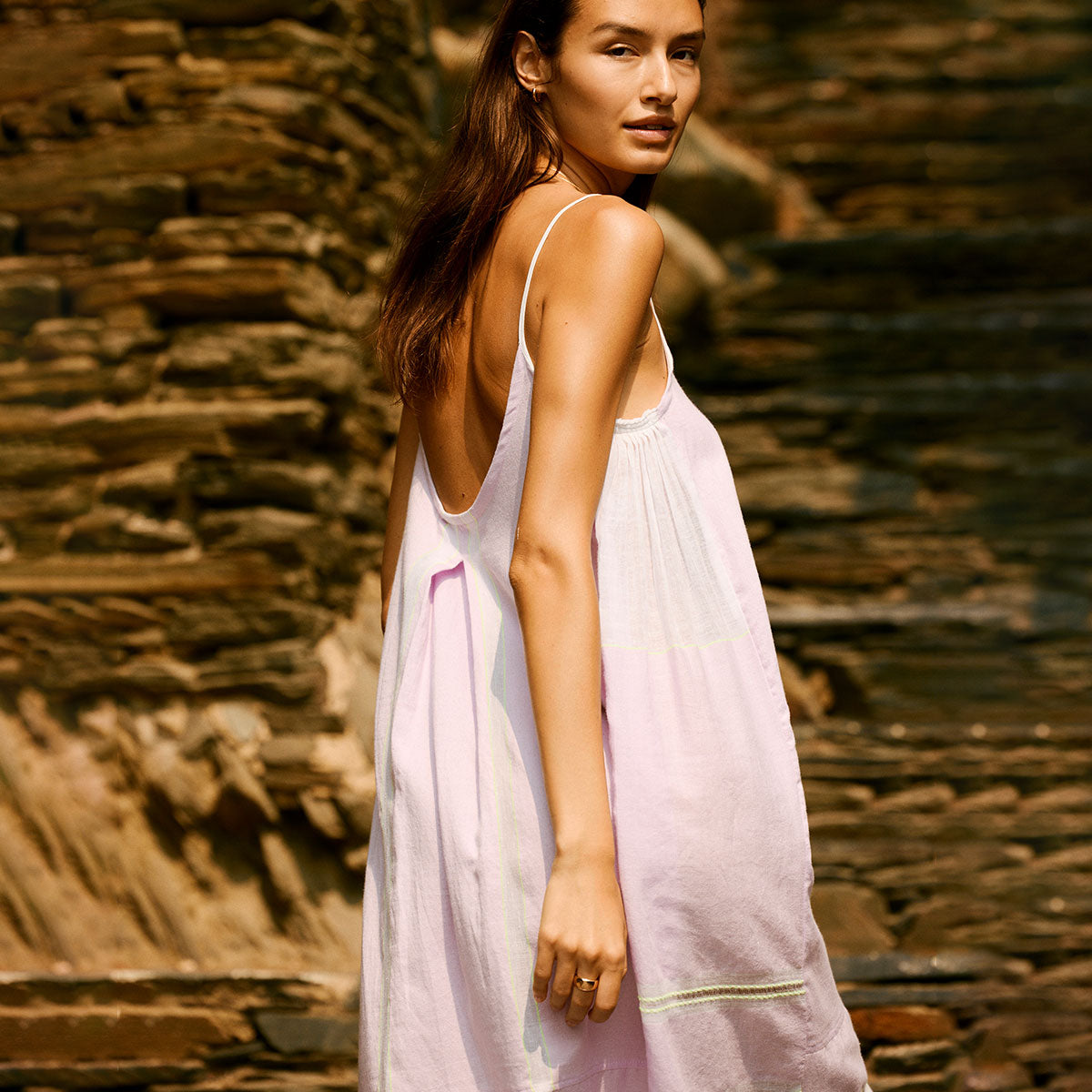 Woman walking on a cliff looking over her shoulder wearing a light pink slip dress. 