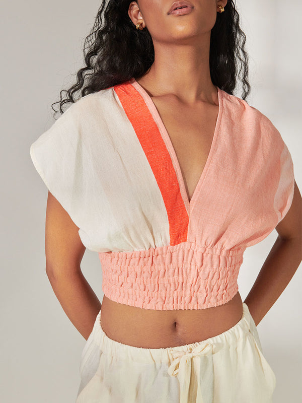 Close up on a Woman Standing Wearing lemlem Alia Plunge Top Featuring asymmetric color block details in tan and blush colors highlighted with bright orange on the soft cream background.