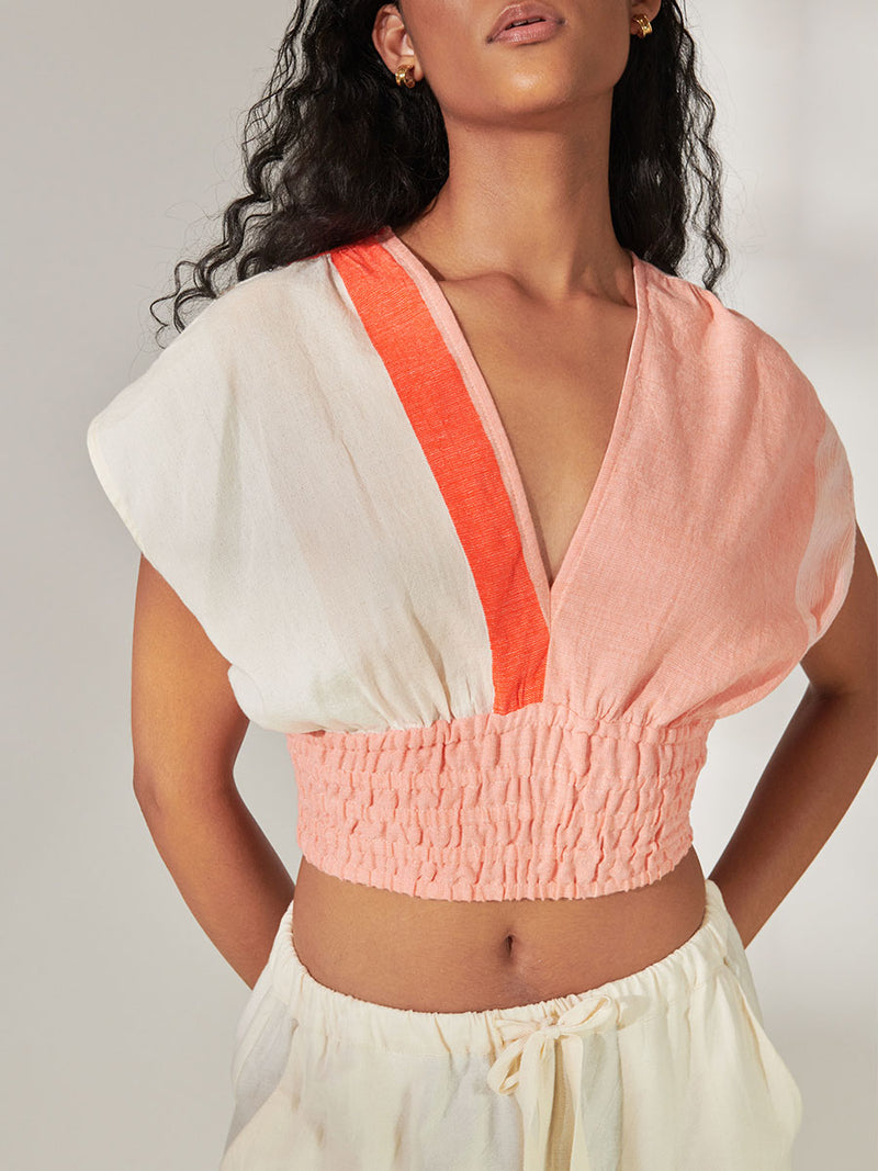 Close up on a Woman Standing Wearing lemlem Alia Plunge Top Featuring asymmetric color block details in tan and blush colors highlighted with bright orange on the soft cream background.