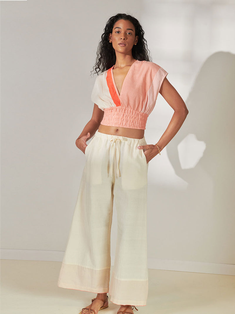 Woman Standing Wearing lemlem Desta Pants Desta Pants Featuring soft cream color and Plunge Top featuring cream and coral colors