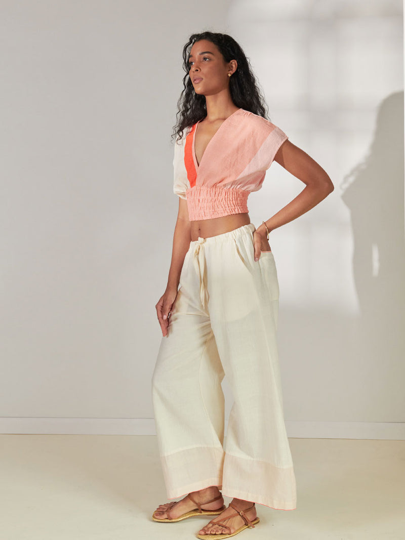 Side View of a Woman Standing Wearing lemlem Desta Pants Desta Pants Featuring soft cream color and Plunge Top featuring cream and coral colors