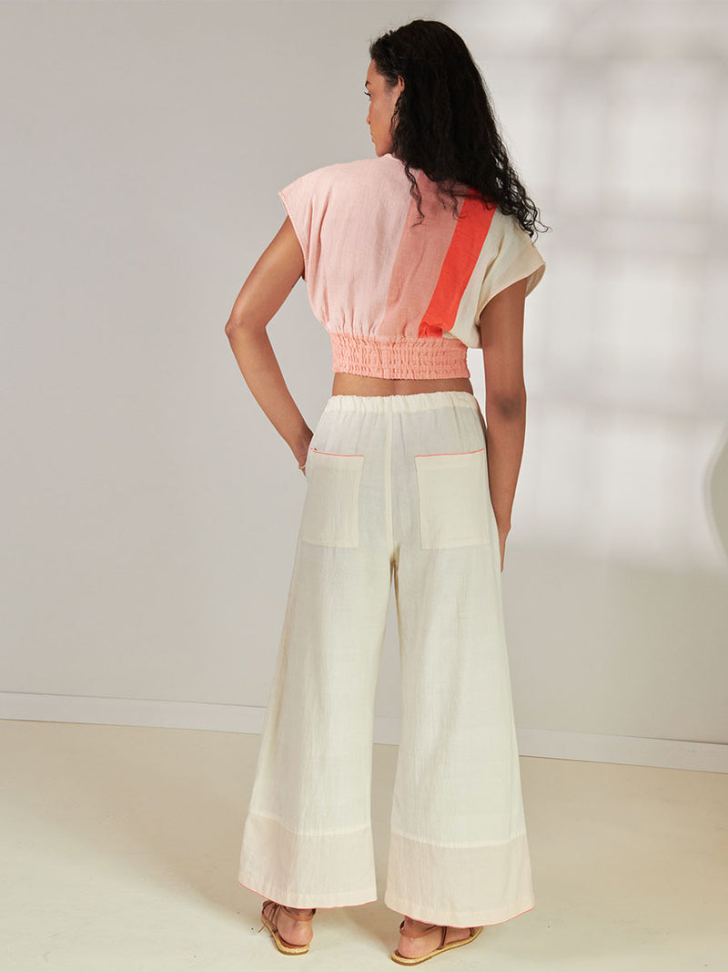 Back View of a Woman Standing Wearing lemlem Desta Pants Desta Pants Featuring soft cream color and Plunge Top featuring cream and coral colors