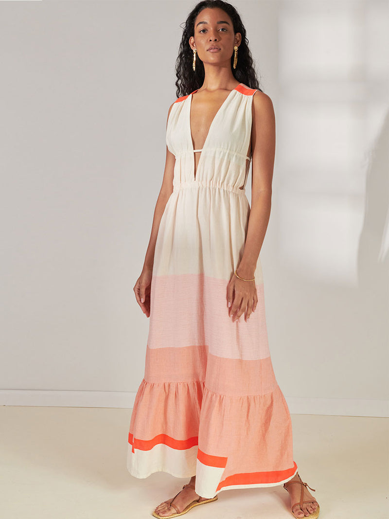 Woman Standing Wearing lemlem Lelisa V Neck Dress Featuring asymmetric color block details in tan and blush colors highlighted with bright orange on the soft cream background.