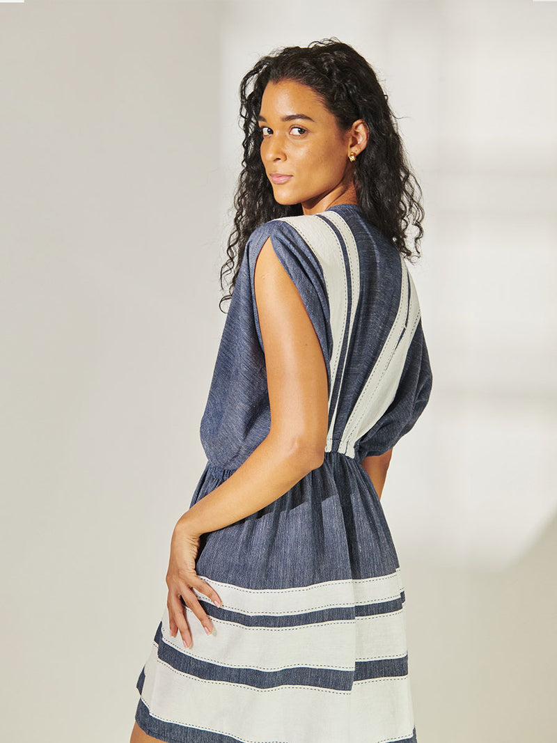 Side View of a Woman Standing Wearing lemlem Alem Plunge Dress featuring Bold Stripe Pattern with pick stitch edge in Classic Navy and White colors.