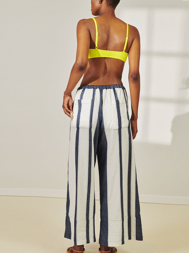 Back View of a Woman Standing Wearing lemlem Desta Pants featuring Bold Stripe Pattern with pick stitch edge in Classic Navy and White colors and Jordanos Citron Scoop Top