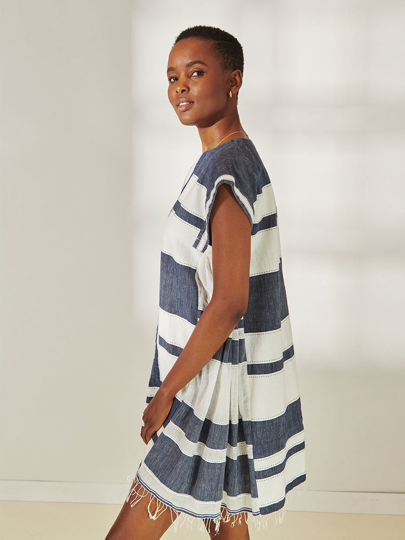 Side View of a Woman Standing Wearing lemlem Elina Caftan Dress featuring Bold Stripe Pattern with pick stitch edge in Classic Navy and White