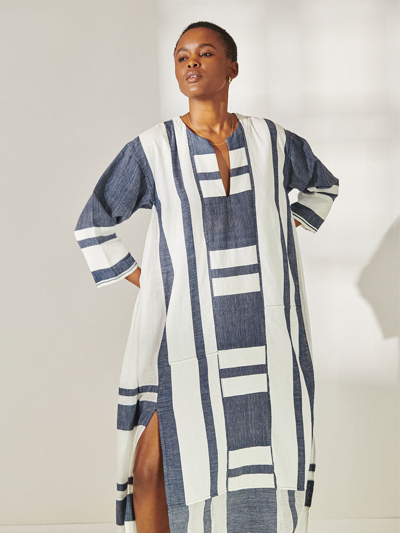 Woman Standing Wearing lemlem Fana Caftan Featuring Bold Stripe Pattern with pick stitch edge in Classic Navy and White colors.