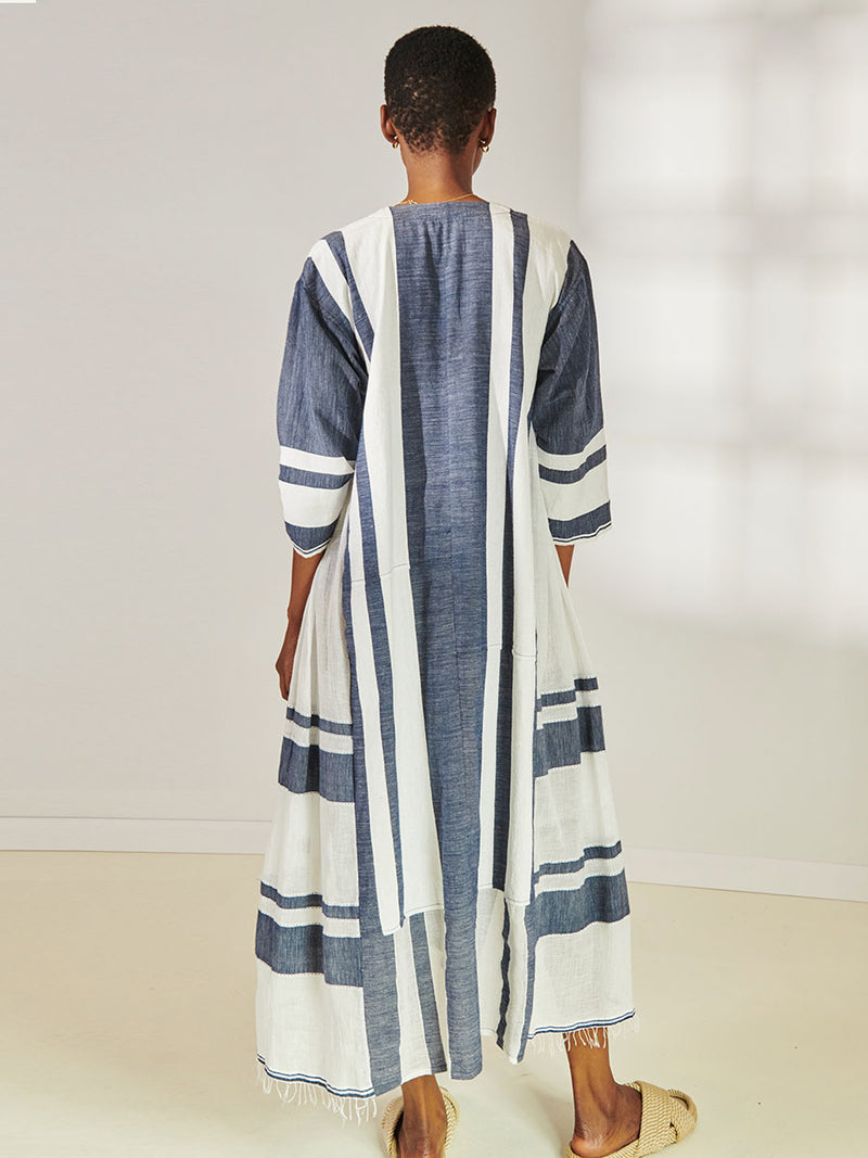 Back View of a Woman Standing Wearing lemlem Fana Caftan Featuring Bold Stripe Pattern with pick stitch edge in Classic Navy and White colors.
