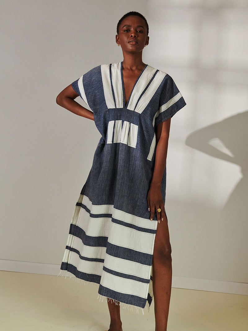 Woman Standing Wearing lemlem Gasira V Neck Caftan Featuring Bold Stripe Pattern with pick stitch edge in Classic Navy and White colors.