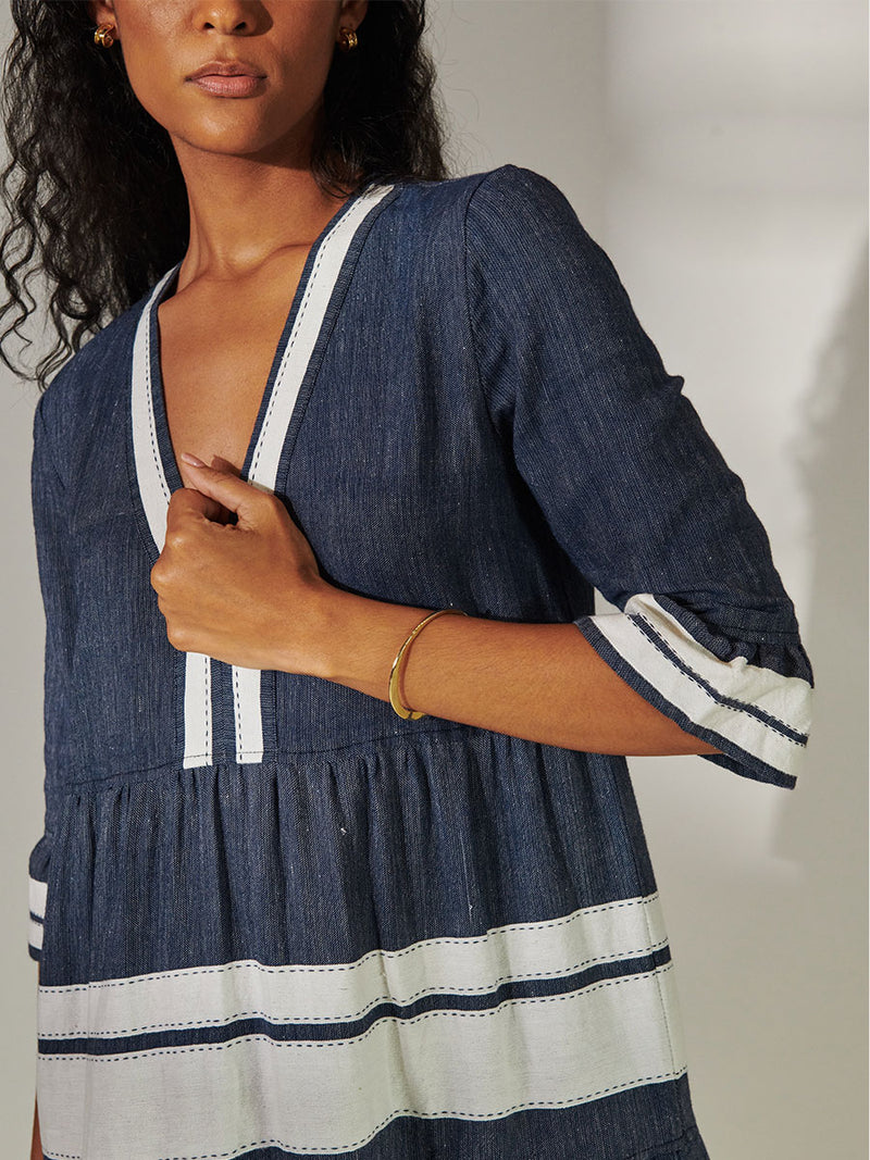 Close up on a Woman Standing Wearing lemlem Hawi Flutter Dress Featuring Bold Stripe Pattern with pick stitch edge in Classic Navy and White colors.
