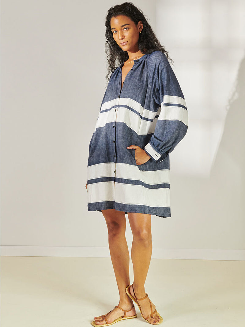 Woman Standing Wearing lemlem Meaza Button Up Dress Featuring Bold Stripe Pattern with pick stitch edge in Classic Navy and White colors.