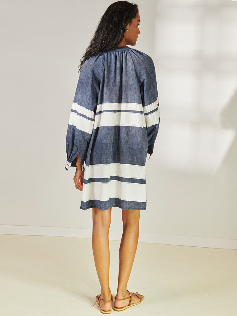 Back View of a Woman Standing Wearing lemlem Meaza Button Up Dress Featuring Bold Stripe Pattern with pick stitch edge in Classic Navy and White colors.