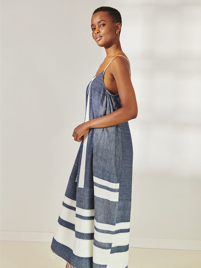 Side View of a Woman Standing Wearing lemlem Nia Slip Dress Featuring Bold Stripe Pattern with pick stitch edge in Classic Navy and White colors.