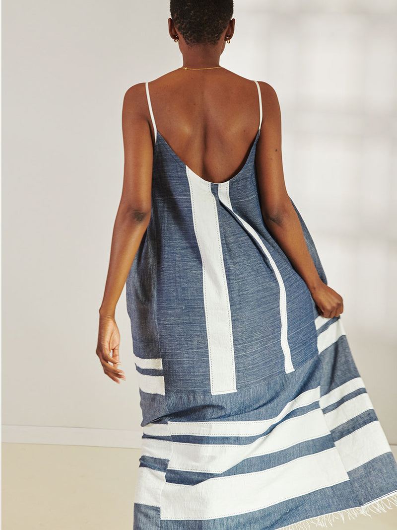 Back View of a Woman Standing Wearing lemlem Nia Slip Dress Featuring Bold Stripe Pattern with pick stitch edge in Classic Navy and White colors.