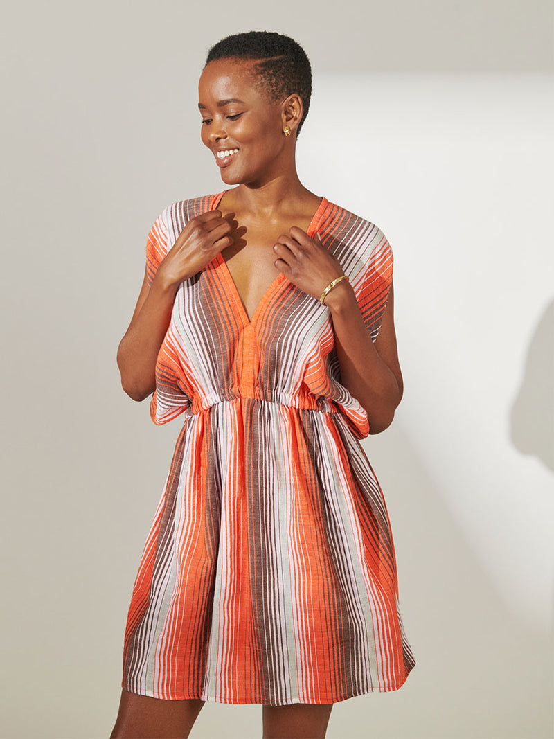 Woman Standing Wearing lemlem  Alem Short Plunge Dress featuring graded continuous stripe pattern creating an ombre effect featuring earth, orchid & burnt orange.