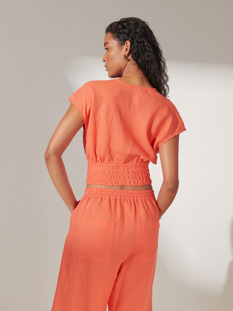 Back View of a Woman standing wearing lemlem Alia Plunge Top in Coral Color and Desta Pants in Coral Color