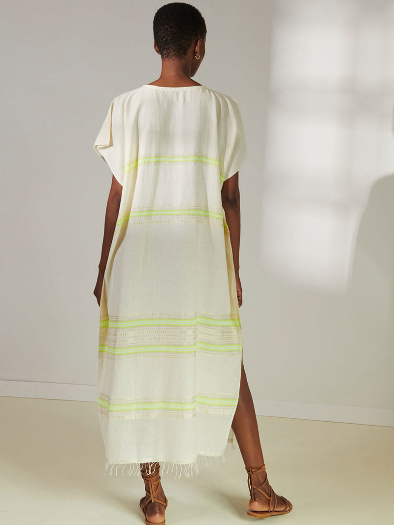 Back View of a Woman Standing Wearing lemlem Dalila Caftan featuring combination of matte and shine natural tibebs and stripes in Vanilla Cream and Lime sorbet colors.