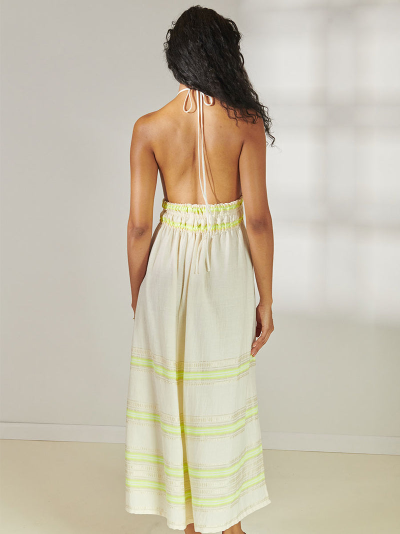 Back View of a Woman Standing Wearing lemlem Gete Triangle Dress featuring combination of matte and shine natural tibebs and stripes in Vanilla Cream and Lime sorbet colors.